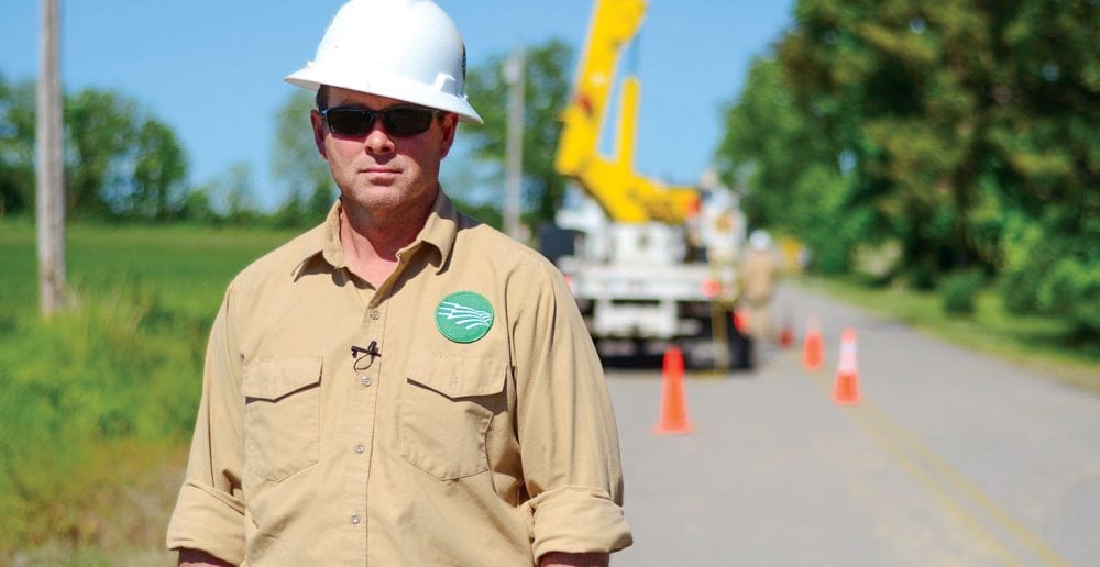 A truck’s flashing lights and the bright cones behind Gibson Electric Membership Corporation Line Crewleader Eugene Stephens are visible warnings to motorists to slow down when approaching the work zone.