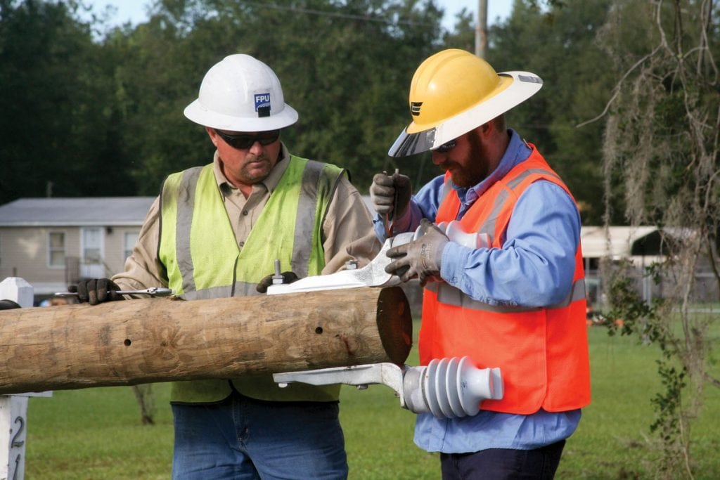 Troy Mitchell of Fayetteville Public Utilities and Cole Woods of Clay Electric Cooperative attach insulators to a new utility pole. (Photograph by Kathy Richardson.)