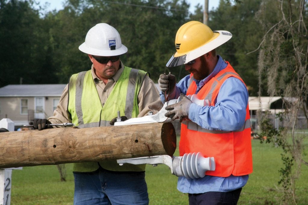 Troy Mitchell of Fayetteville Public Utilities and Cole Woods of Clay Electric Cooperative attach insulators to a new utility pole. (Photograph by Kathy Richardson.) 